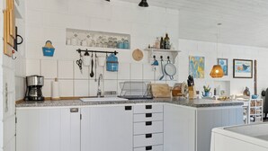 Une cuisine avec des meubles blancs, une machine à café et divers ustensiles.