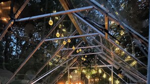 Un espace intime et clos, doté d’un plafond en verre, aménagé avec des chaises et des tables, et décoré de guirlandes lumineuses et de bougies.