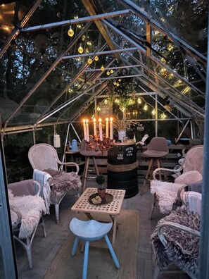 Ein gemütlicher, abgeschlossener Raum mit Glasdecke, ausgestattet mit Stühlen und Tischen, dekoriert mit Lichterketten und Kerzen.
