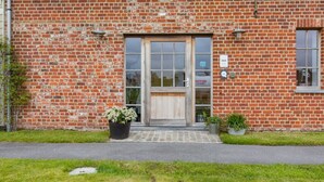 A brick building with a wooden door and windows, a small garden area with potted plants, and a sign indicating 'B&B'. - Xtra space Deluxe room 1st floor (Ieper)