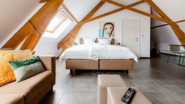 A bedroom with a sloped ceiling, a large bed, a sofa, and a painting on the wall. - Xtra space Deluxe room 1st floor (Ieper)