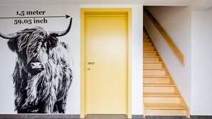 A yellow door with a mural of a yak, a staircase, and a measurement sign indicating the door's height. - Xtra space Deluxe room 1st floor (Ieper)