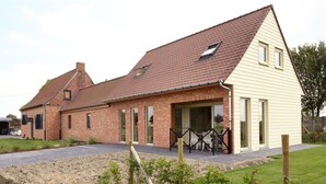 Een twee verdiepingen tellend bakstenen huis met een schuin dak, een overdekte patio en een omheinde tuin.