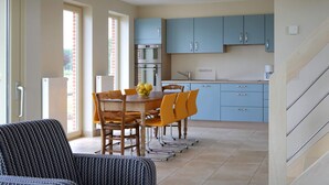 Een moderne keuken met blauwe kastjes, een eettafel met stoelen, en een trap naar een hoger gelegen verdieping.
