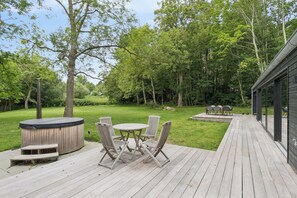A wooden deck with a hot tub, outdoor seating, and a view of a forested area. - Bright holiday home near Ordrup (Fårevejle)