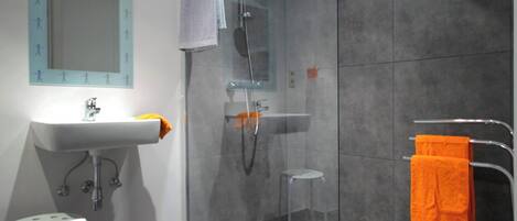 Une salle de bain moderne avec une douche à parois de verre, un lavabo blanc et un petit tabouret.