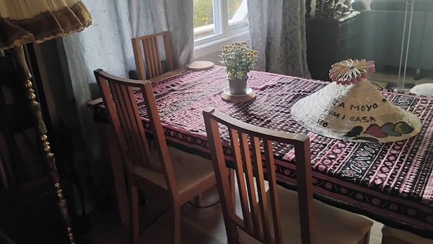 Et spiseområde med et rundt bord dækket af en farverig dug, omgivet af træstole.