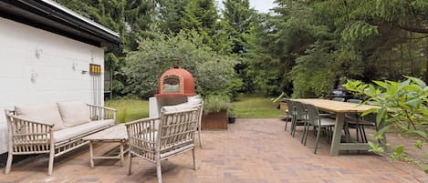 A patio with a brick floor, a wooden table, and a wicker sofa.