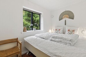 Een slaapkamer met een bed, een raam, een stoel en een ventilator bevestigd aan de muur.