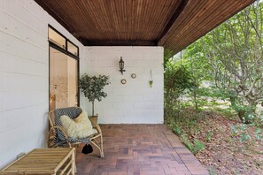 A covered patio with a wicker chair, a small table, and a potted plant.
