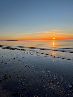 Une plage au coucher du soleil, avec une eau calme et un ciel dégagé.