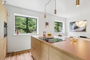 Une cuisine moderne dotée de grandes fenêtres, d’un îlot central, de luminaires suspendus et d’une œuvre d’art encadrée au mur.
