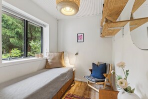 A bedroom with a bed, a chair, a window, and a wall-mounted shelf. - Modernised 70s cottage in forest near beach (Nykøbing Sjælland)