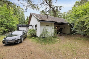 Une maison devant laquelle est garée une voiture, le tout entouré d’arbres.