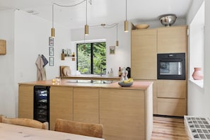 A modern kitchen with wooden cabinets, a built-in oven, and pendant lighting. - Modernised 70s cottage in forest near beach (Nykøbing Sjælland)
