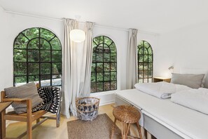 A room with a bed, a chair, a wicker basket, and large arched windows. - Modernised 70s cottage in forest near beach (Nykøbing Sjælland)