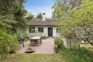 A house with a brick patio, a wooden table, and potted plants. - Modernised 70s cottage in forest near beach (Nykøbing Sjælland)