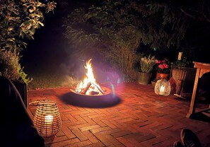 A fire pit in a brick patio area surrounded by potted plants and a lantern. - Modernised 70s cottage in forest near beach (Nykøbing Sjælland)