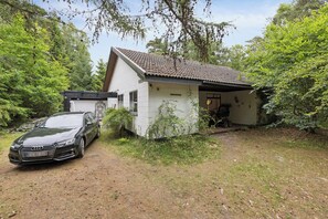 A house with a car parked in front, surrounded by trees. - Modernised 70s cottage in forest near beach (Nykøbing Sjælland)