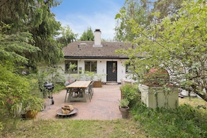 A house with a brick patio, a wooden table, and potted plants.