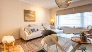 Una sala de estar moderna con sofá, sillón, mesa de centro de vidrio y un ventanal grande.