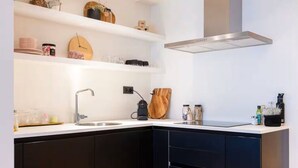 Una cocina moderna con un lavaplatos integrado, armarios negros, una campana extractora de acero inoxidable y una tabla de cortar de madera en la encimera.