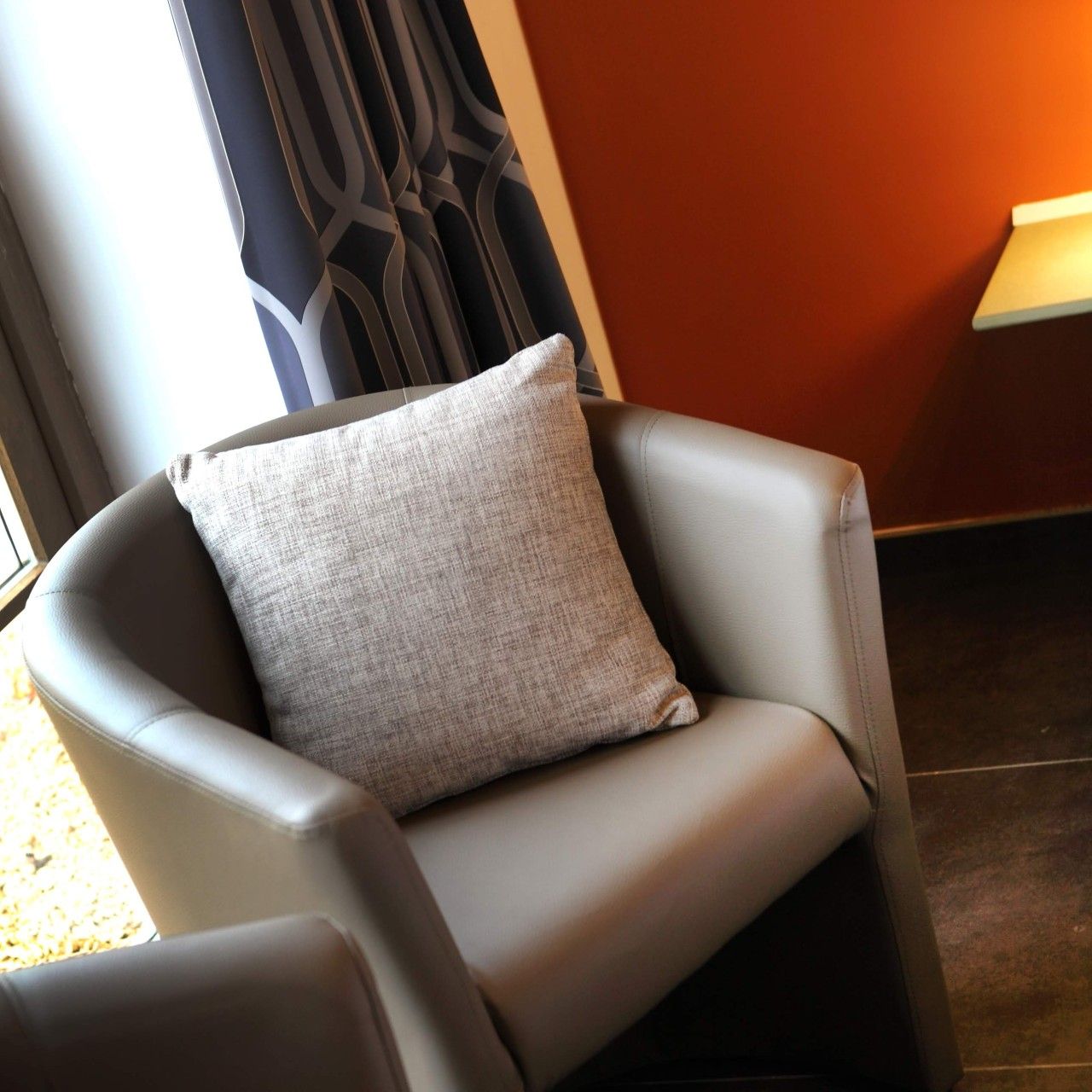 Une chaise avec un coussin à texture particulière, dans une pièce dont le mur est de couleur sombre et qui possède une fenêtre.