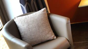 Une chaise avec un coussin à texture particulière, dans une pièce dont le mur est de couleur sombre et qui possède une fenêtre.