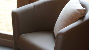 Un fauteuil en cuir marron avec un coussin, placé près d’une fenêtre donnant sur une cour.