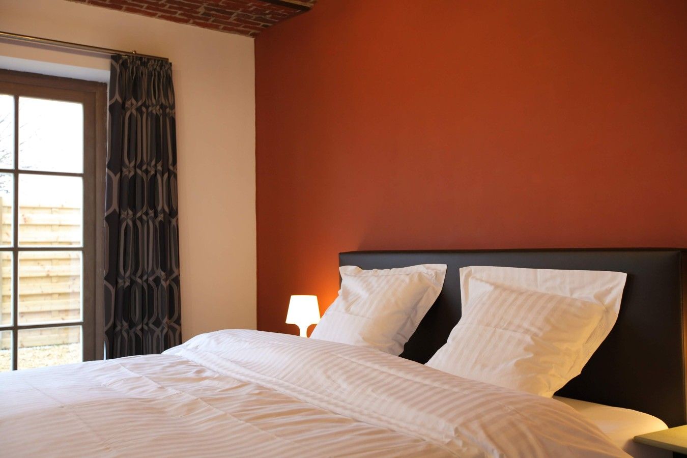 Een hotelkamer met een bed, nachtkastje, lamp en een raam met gordijnen.