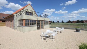 A building with a sloped roof and large windows, surrounded by a gravel area with white chairs. - Ground floor Standard room - Musterd (Ieper)