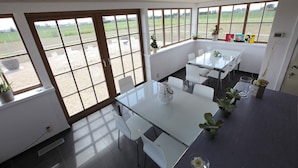 A spacious dining area with large windows, white furniture, and potted plants. - Ground floor Standard room - Musterd (Ieper)