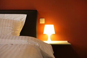 A neatly made bed with white linens and a pillow, positioned next to a bedside table with a lamp. - Ground floor Standard room - Musterd (Ieper)