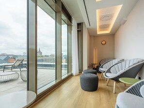 A modern hotel room with large windows, a view of the city, a round ottoman, and wicker chairs. - ScanHotels Apartments (Rostock)