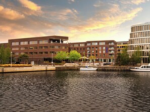 A waterfront building with a dock, a boat, and a clear sky. - ScanHotels Apartments (Rostock)