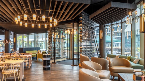 A modern interior with wooden flooring, leather seating, and a wall of hanging bottles.