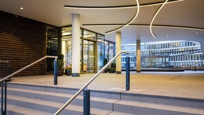 A modern building entrance with a staircase, glass doors, and a view of another building.