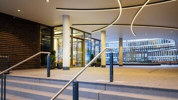 Ein moderner Gebäudeeingang mit Treppe, Glasüren und Blick auf ein anderes Gebäude.