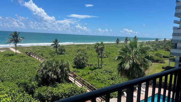 A balcony with a view of a beach, palm trees, and a pool. - Oceanfront Sanctuary with 3 bedrooms (Fort Pierce)