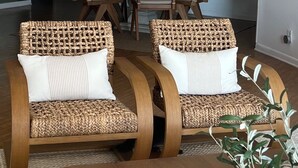 Two wicker chairs with white cushions, a wooden table, and a plant in a modern room. - Oceanfront Sanctuary with 3 bedrooms (Fort Pierce)