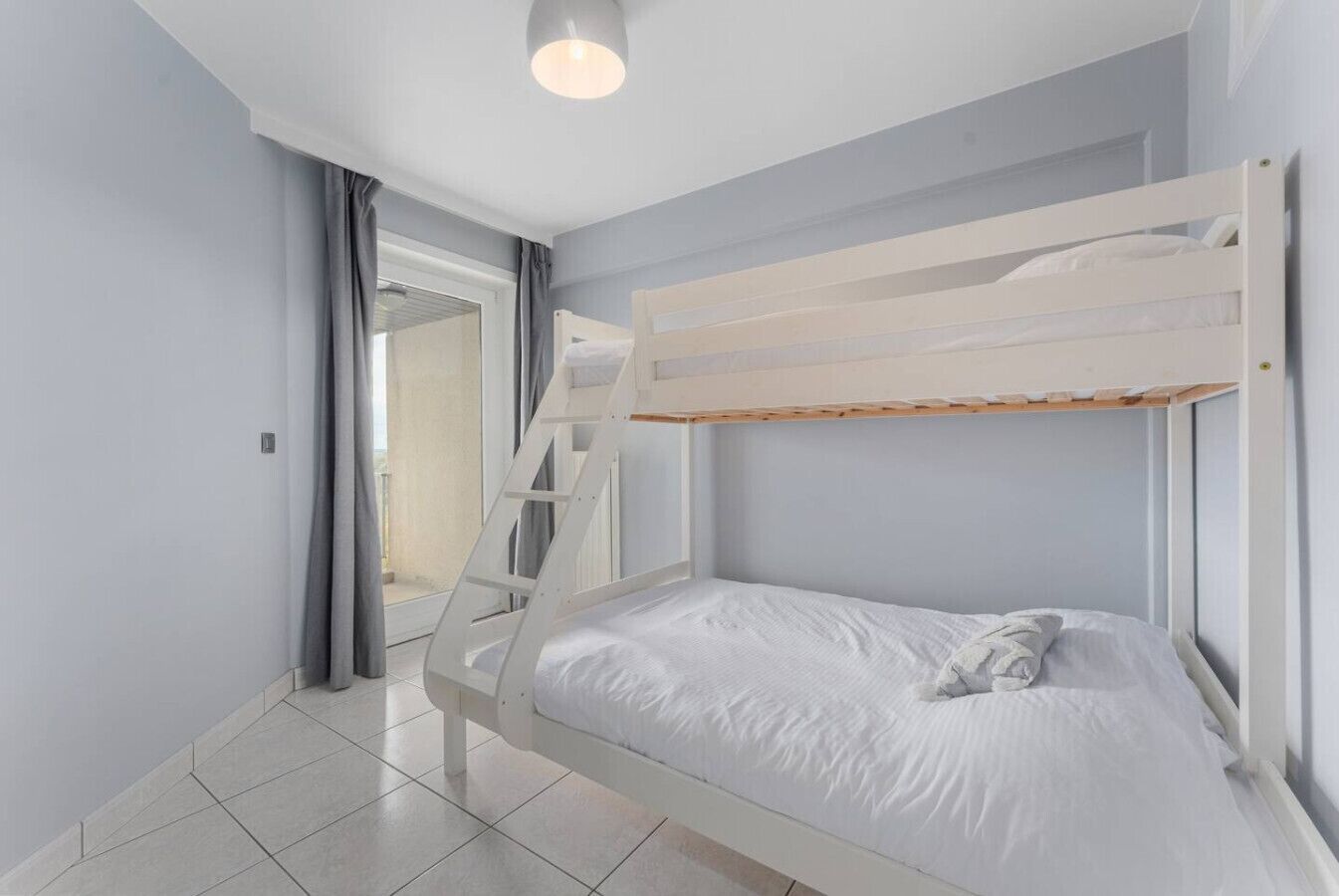Habitació amb lliteres, roba de llit blanca i vista a un balcó per una porta.