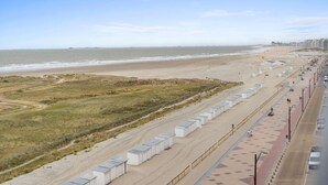 Ett hotell vid stranden med en lång rad rum som ligger längs strandlinjen, en sandstig som leder ner till stranden och en parkeringsplats med några få bilar.