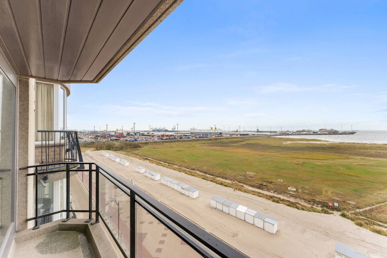 Un balcon offrant une vue sur une zone côtière, notamment une plage et des bâtiments industriels.