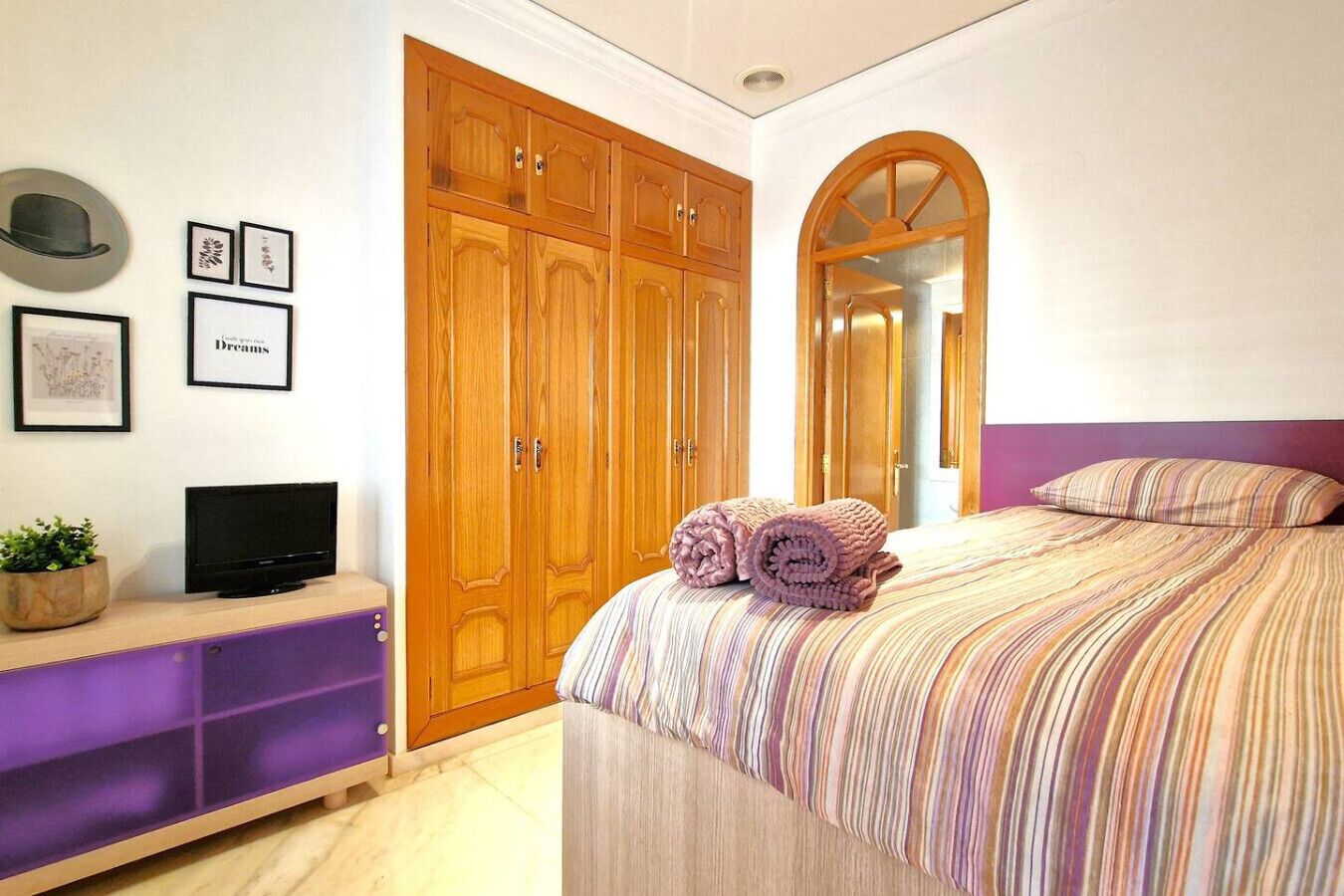 Ein Schlafzimmer mit Bett, Fernseher, Kleiderschrank und Spiegel.
