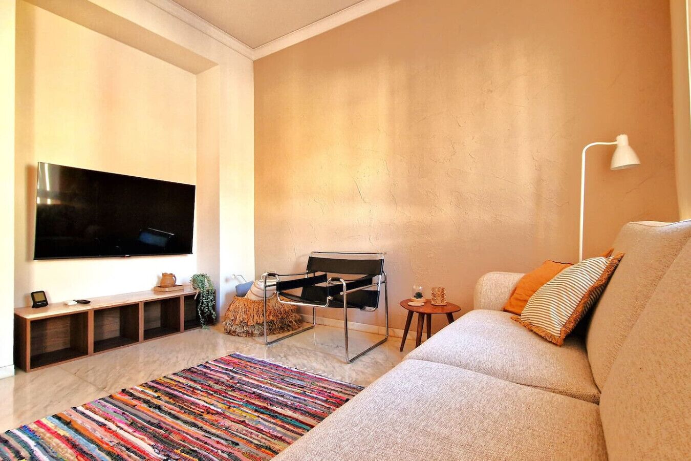 A modern living room with a flat-screen TV, a sofa, a colorful rug, and a minimalist chair.