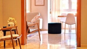 Ein modernes Wohnzimmer mit einer Couch, einem Holzstuhl, einem schwarzen Hocker und einem Essbereich mit Tisch und Stühlen.