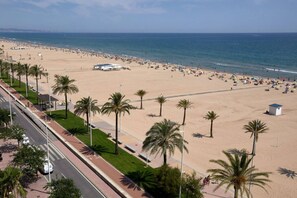 A beach with palm trees, a road, and a building.