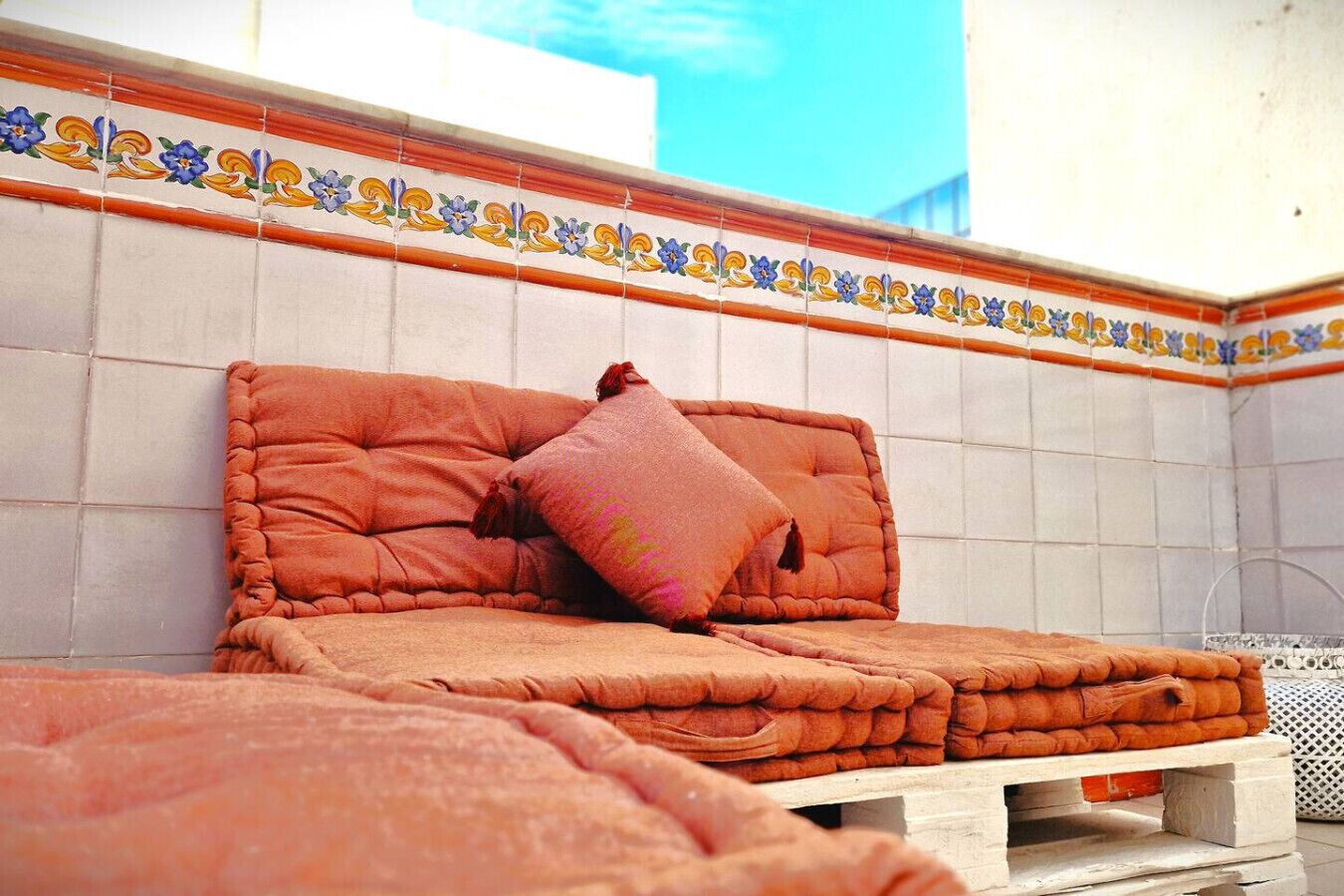 A bed with a tufted headboard and a single pink pillow, set against a tiled wall with a decorative border.