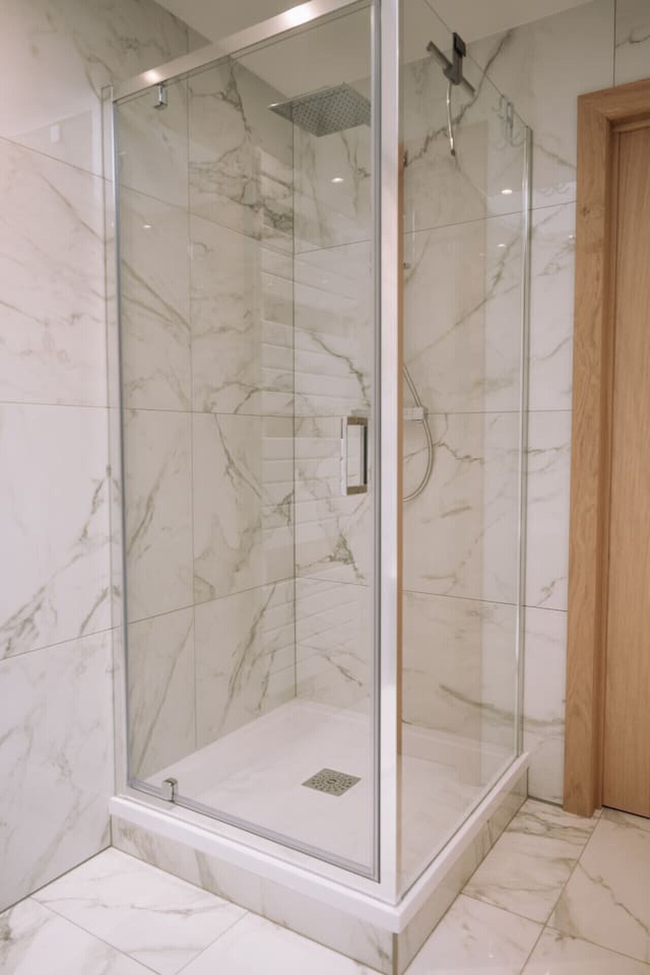 Ducha con cerramiento de vidrio, paredes y piso de mármol.