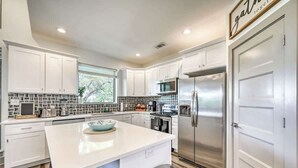 Een moderne keuken met witte kasten, een centraal eiland, roestvrijstalen apparatuur en uitzicht op de omgeving.